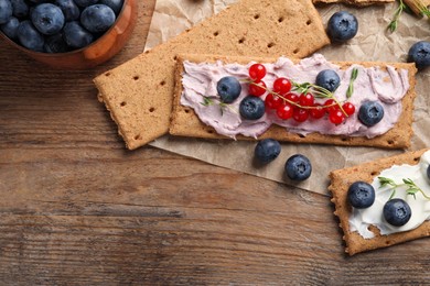 Photo of Tasty crispy crackers with cream cheese, thyme and berries, flat lay. Space for text