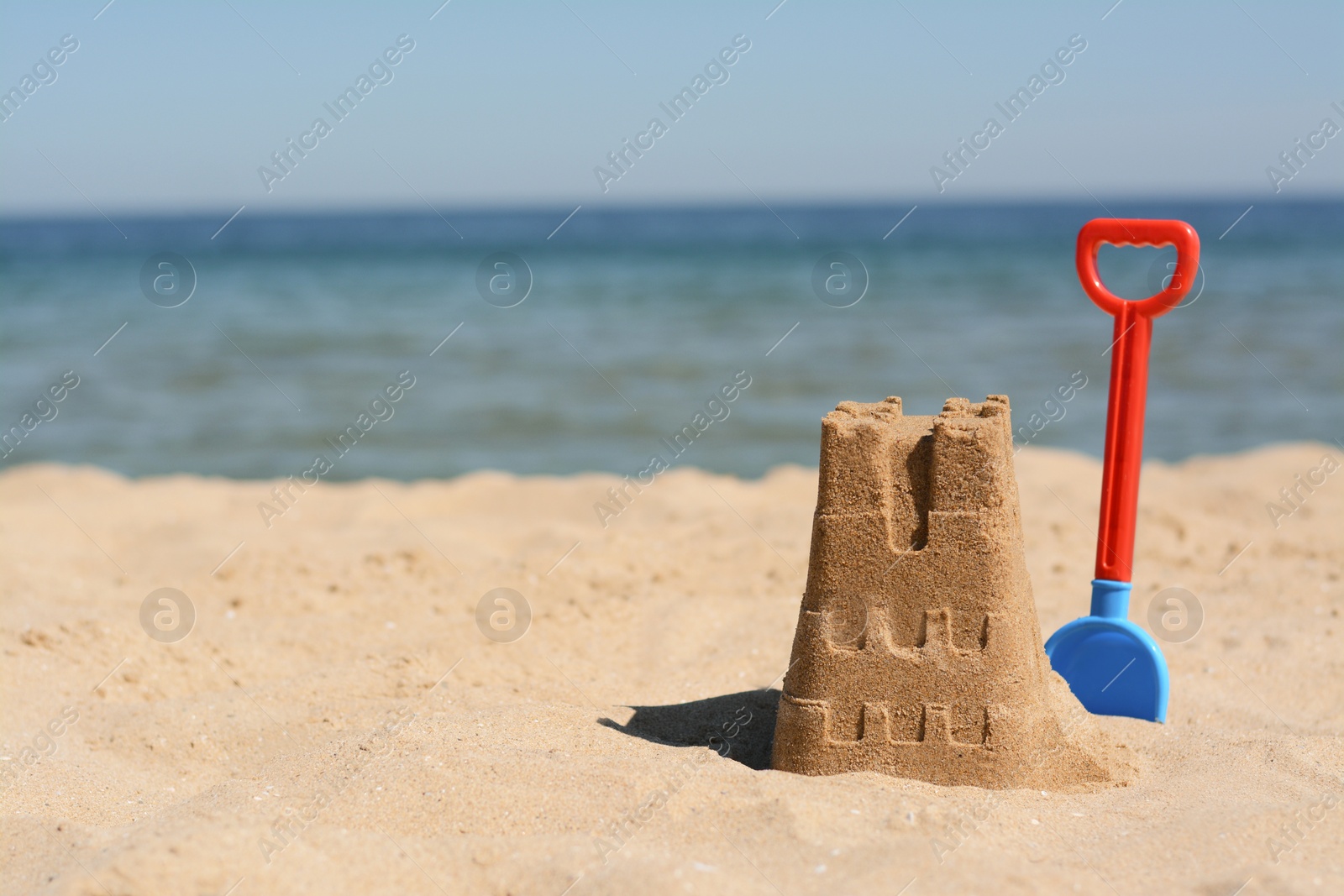 Photo of Sand castle and child plastic shovel on beach near sea. Space for text