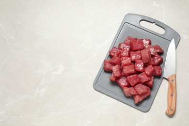 Photo of Cooking delicious goulash. Raw beef meat and knife on light grey table, top view. Space for text