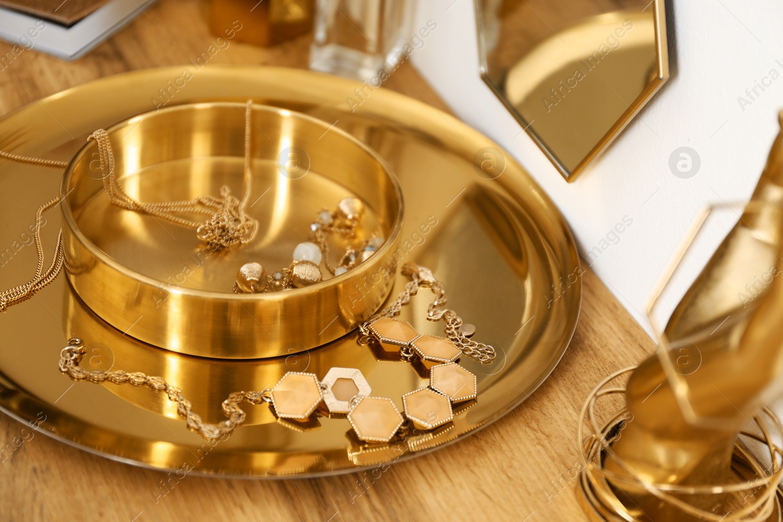 Photo of Composition with gold accessories and jewelry on dressing table near white wall