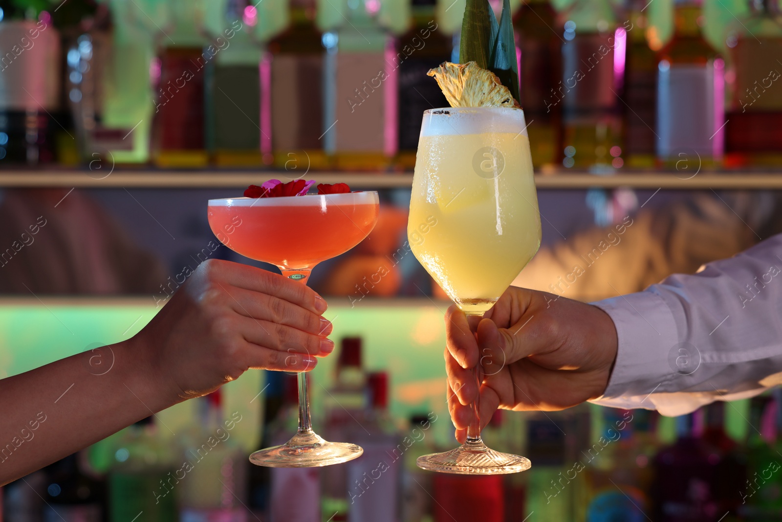 Photo of Man and woman holding glasses with fresh alcoholic cocktails in bar, closeup