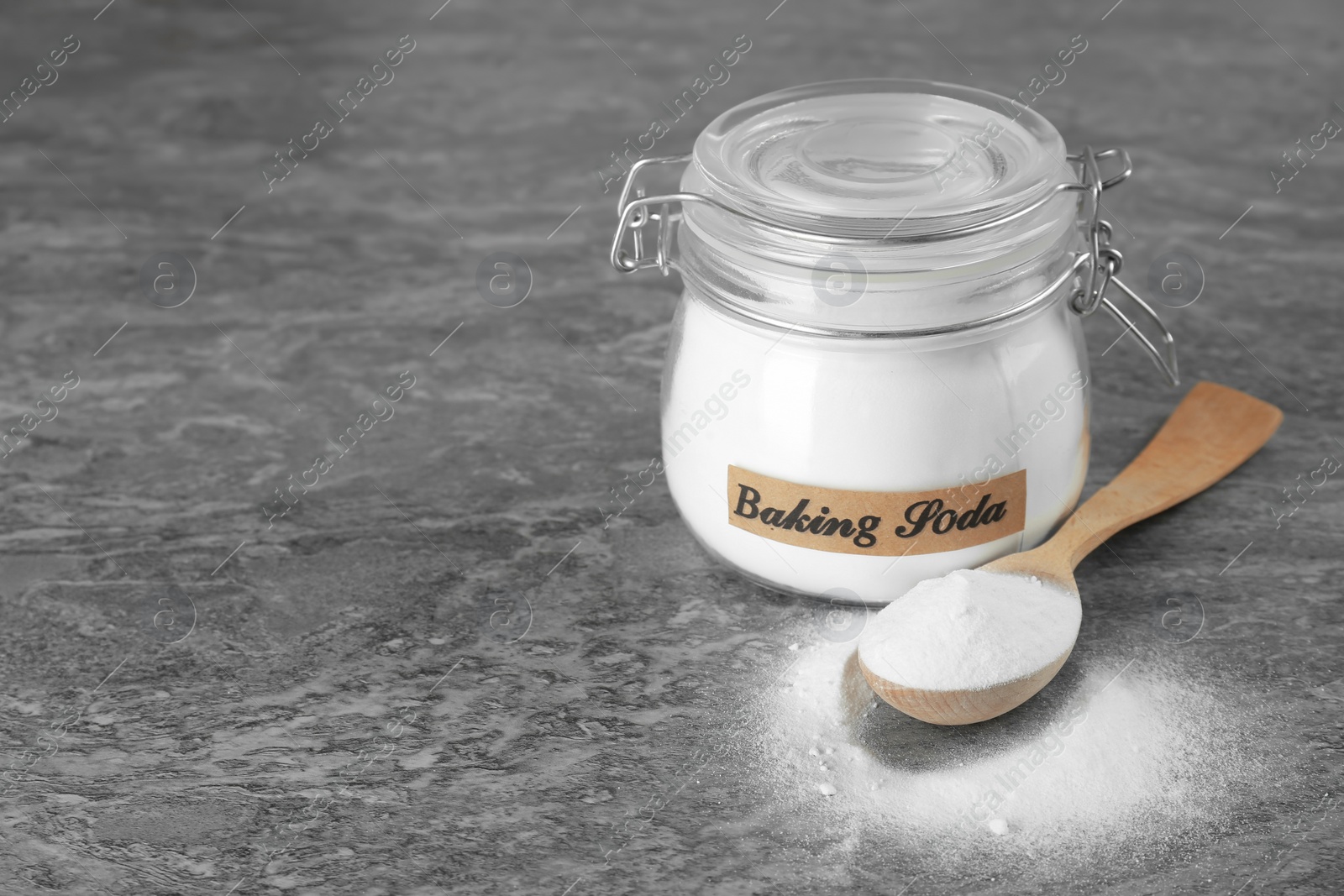 Photo of Wooden spoon and jar with baking soda on grey table. Space for text
