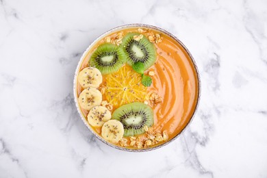 Photo of Bowl of delicious fruit smoothie with fresh banana, kiwi slices and granola on white marble table, top view