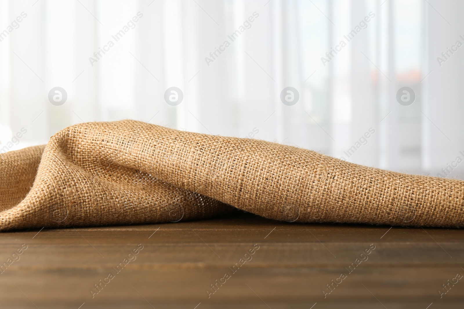 Photo of Brown burlap fabric on wooden table, closeup. Space for text