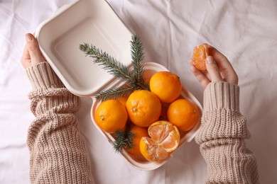 Woman with delicious ripe tangerines on white bedsheet, top view