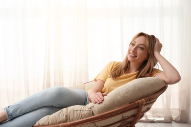 Photo of Beautiful young woman relaxing in papasan chair indoors, space for text