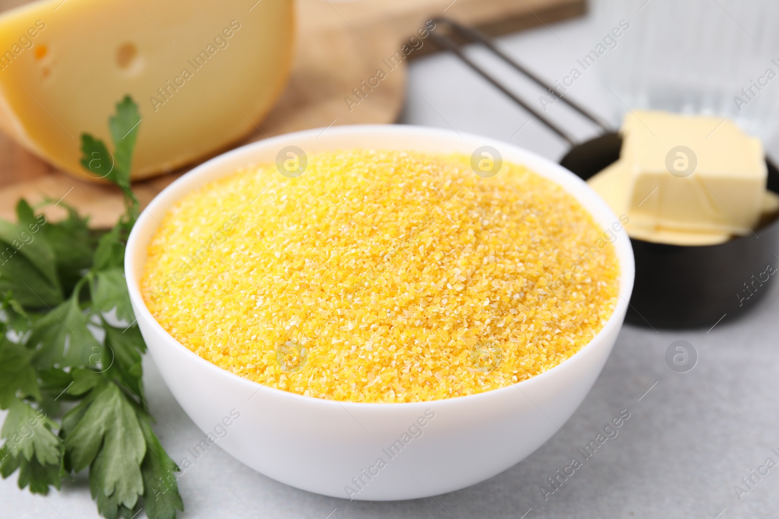 Photo of Raw cornmeal in bowl, parsley, cheese and butter on light table, closeup