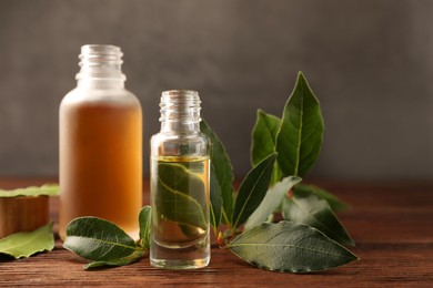 Bottles of bay essential oil and fresh leaves on wooden table