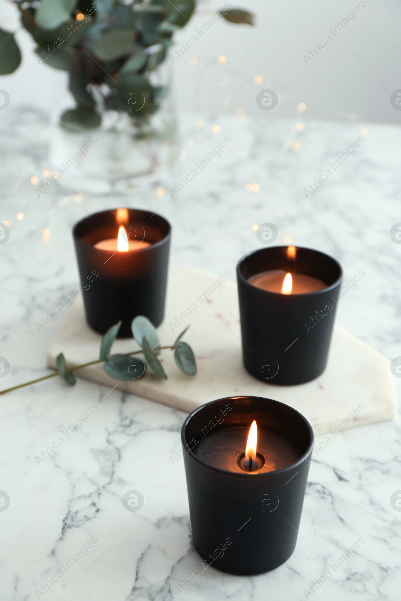 Photo of Burning candles and green branch on marble table
