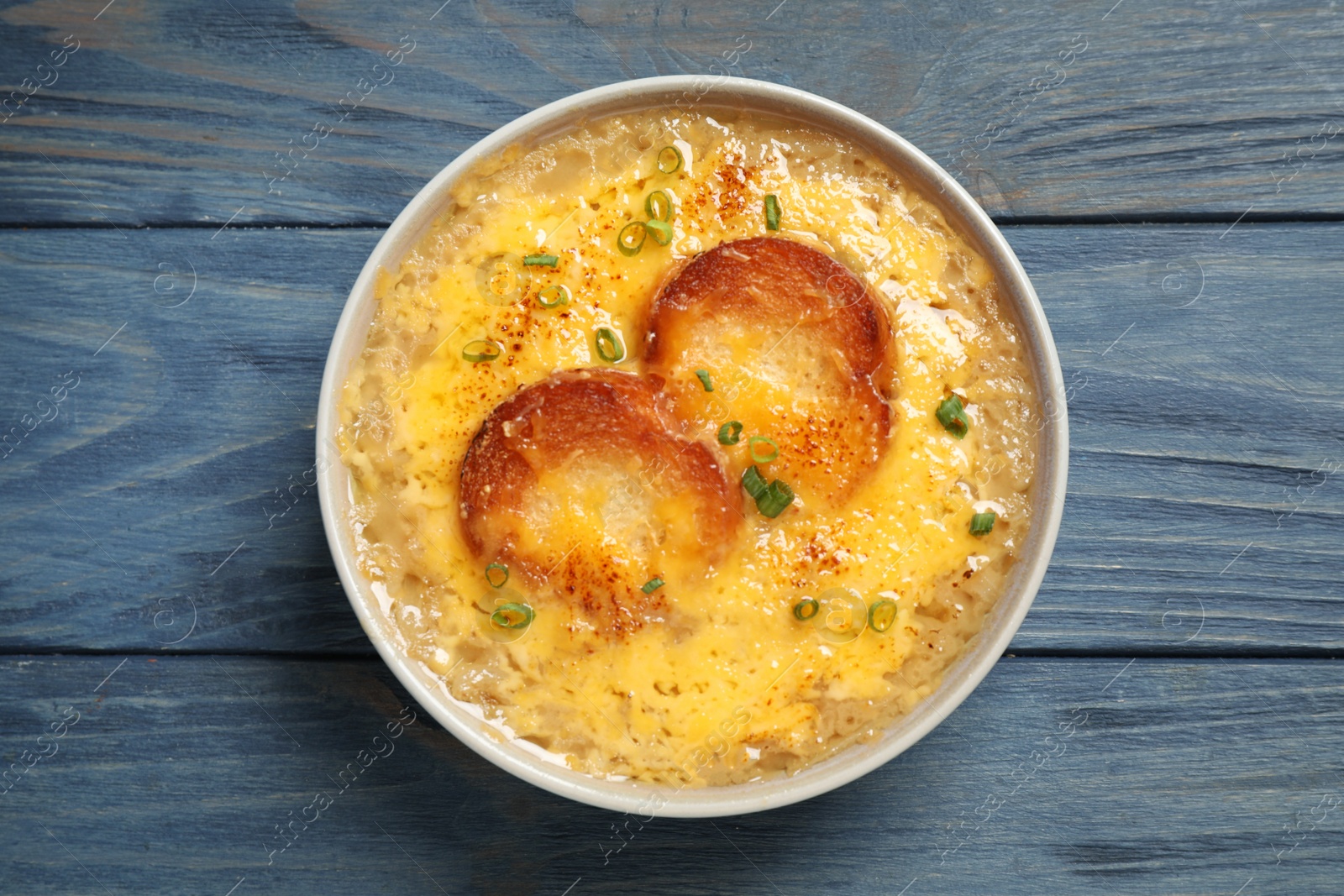 Photo of Tasty homemade french onion soup on blue wooden table, top view