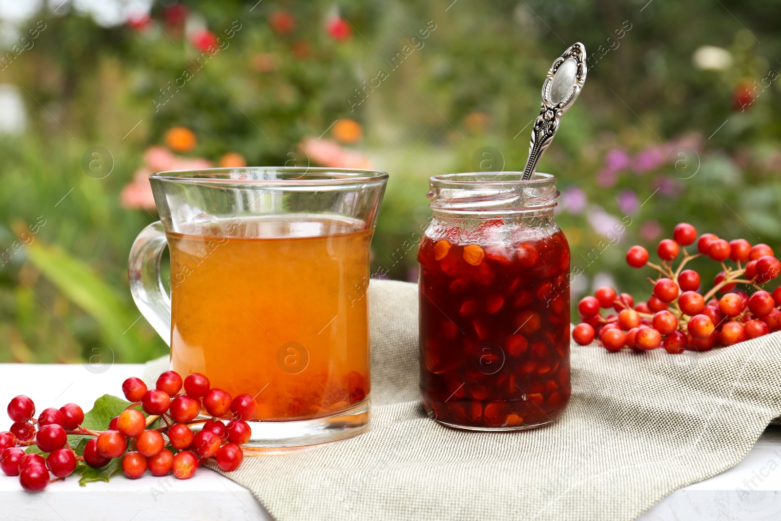 Photo of Cup of tea, jam and ripe viburnum berries on white wooden table outdoors