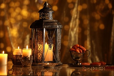 Photo of Arabic lantern, burning candles, dates and misbaha on mirror surface against blurred lights