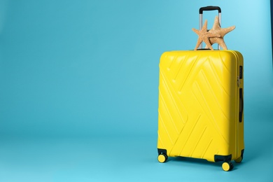 Stylish suitcase with sea stars on color background. Space for text