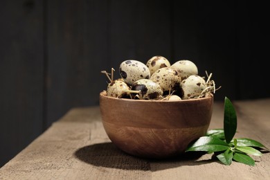 Photo of Bowl with quail eggs and green leaves on wooden table, closeup