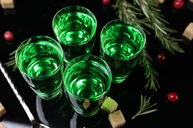 Photo of Absinthe in shot glasses, cranberries, rosemary and brown sugar on mirror table, closeup. Alcoholic drink