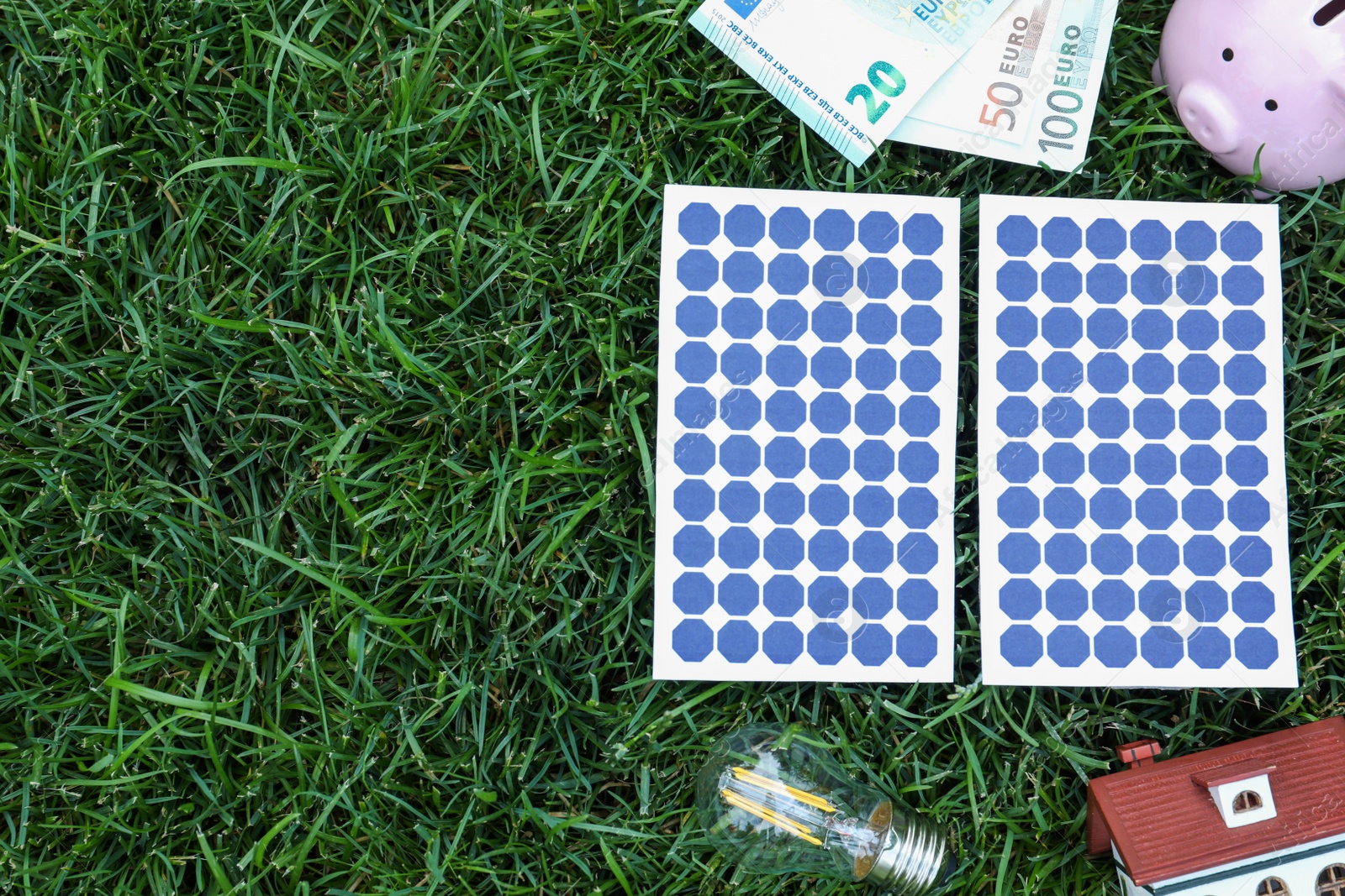 Photo of Flat lay composition with solar panels, house model and money on green grass. Space for text