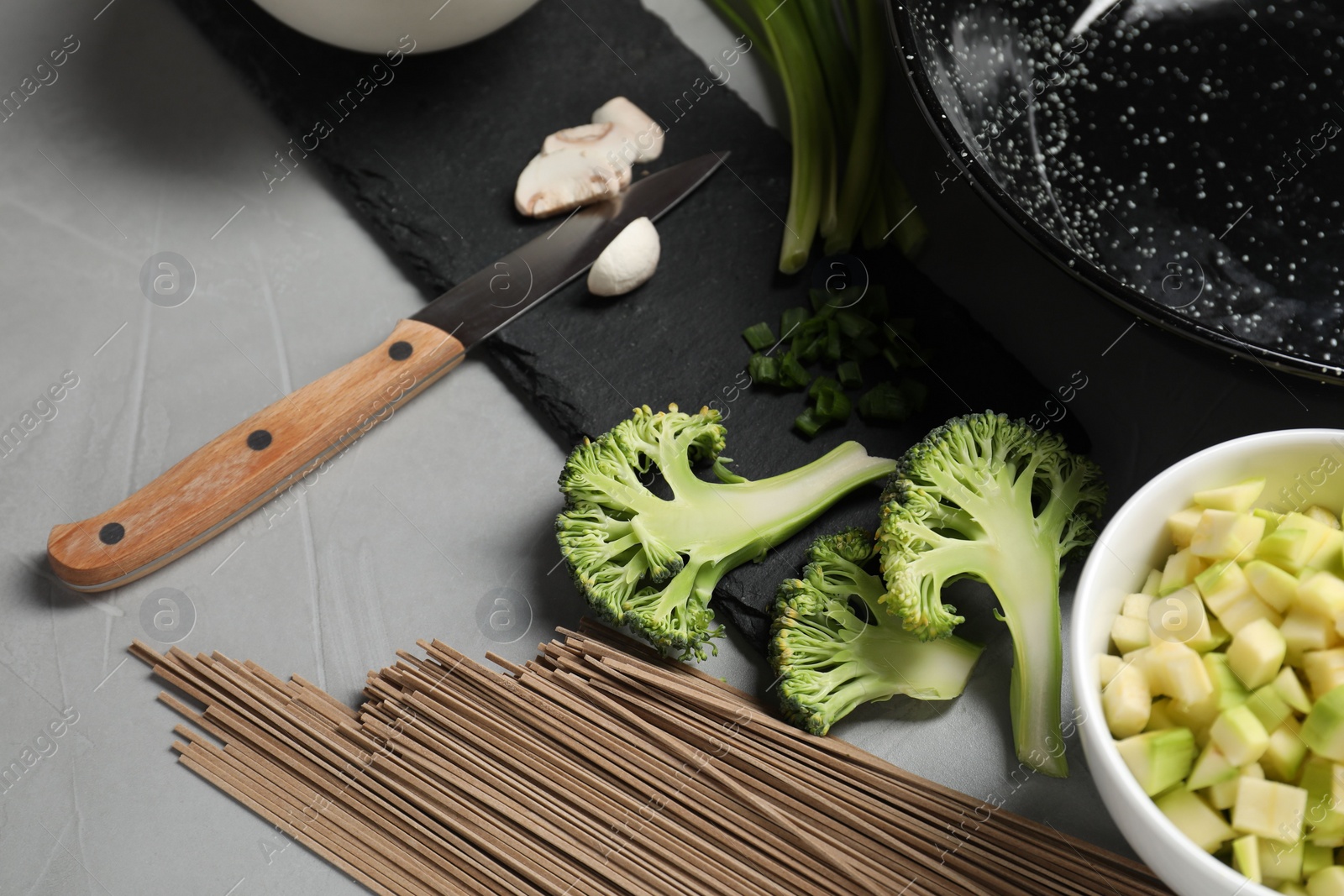 Photo of Wok pan, noodles and different vegetables on light grey table