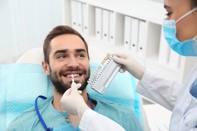 Photo of Dentist matching young man's teeth color with palette in office