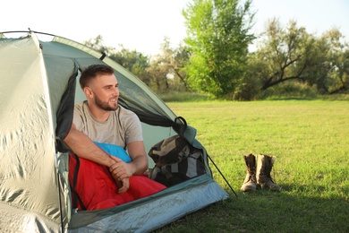 Young man in sleeping bag sitting inside camping tent