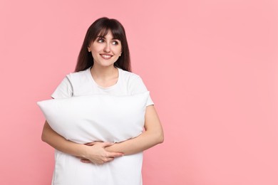 Photo of Happy woman in pyjama holding pillow on pink background, space for text