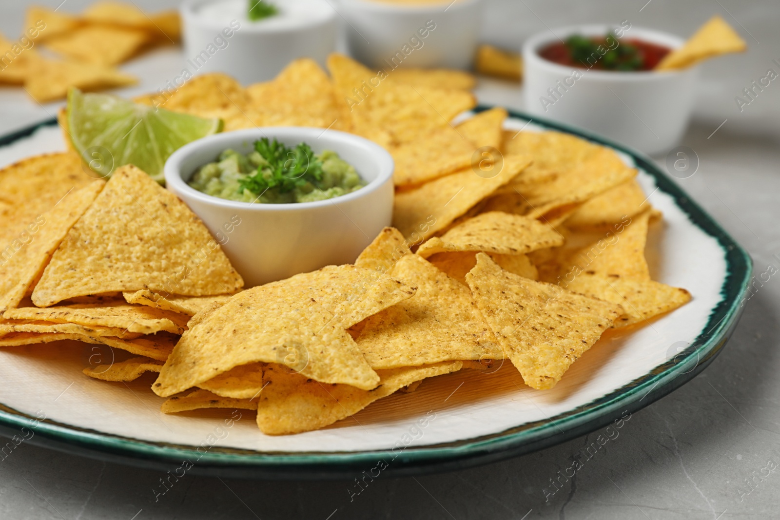 Photo of Plate of Mexican nacho chips with sauce on grey marble table, closeup