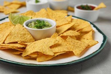 Photo of Plate of Mexican nacho chips with sauce on grey marble table, closeup