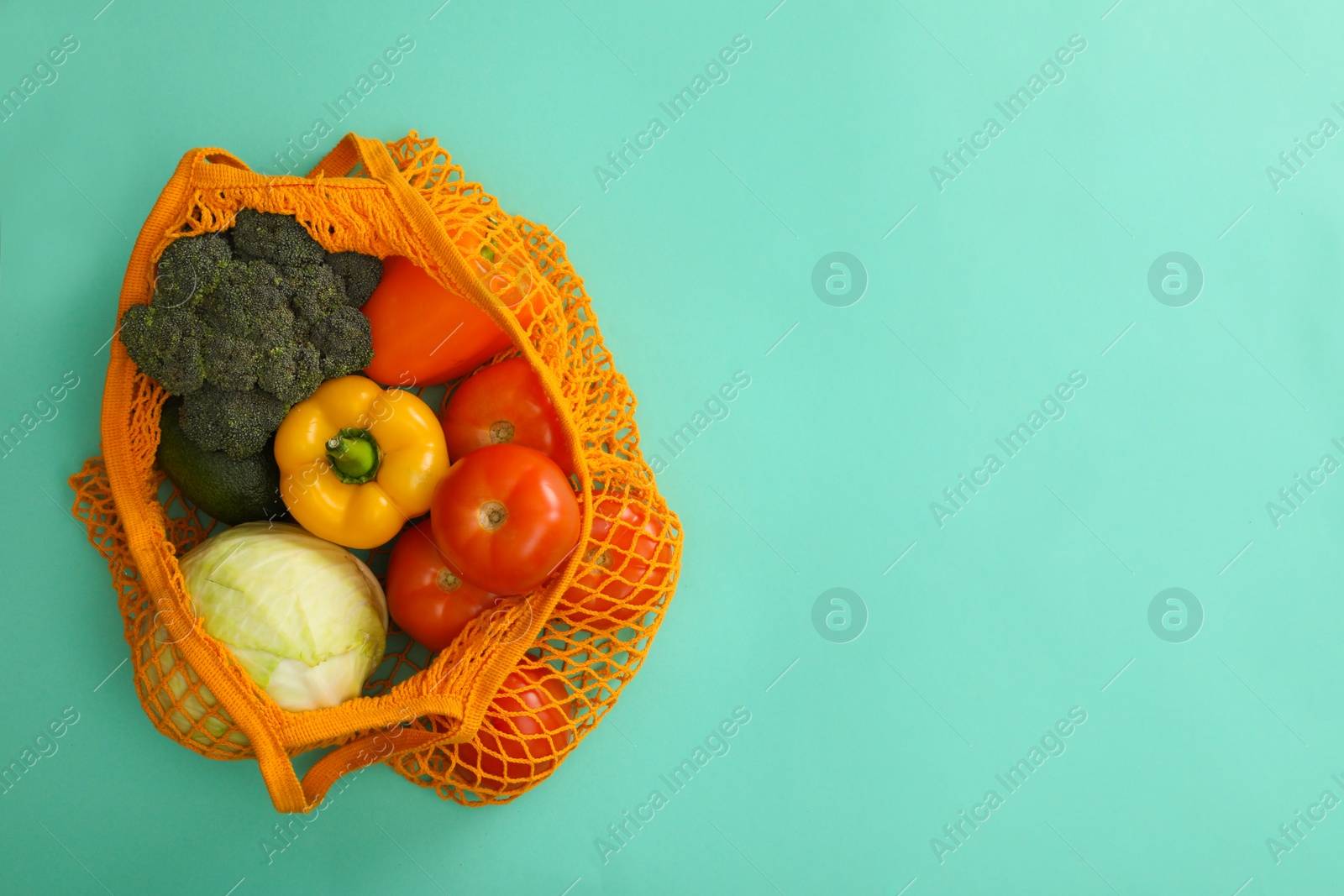 Photo of Net bag with vegetables on turquoise background, top view. Space for text