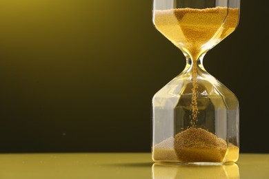Photo of Hourglass with flowing sand on table against color background, closeup. Space for text