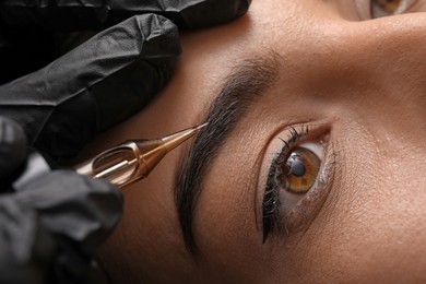 Young woman undergoing procedure of permanent eyebrow makeup in tattoo salon, closeup