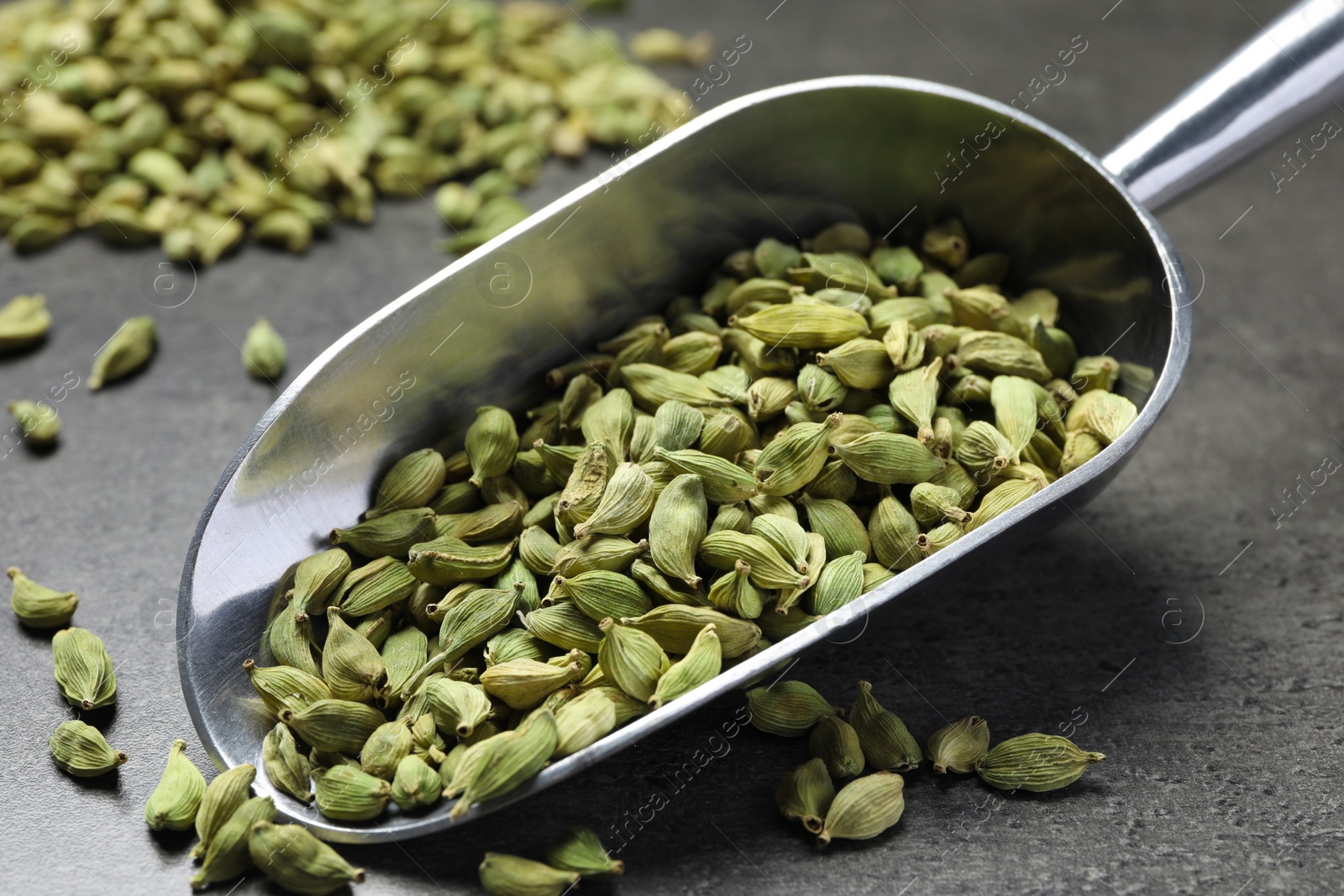 Photo of Scoop with dry cardamom pods on dark grey table, closeup