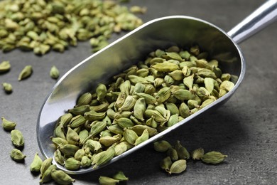Photo of Scoop with dry cardamom pods on dark grey table, closeup