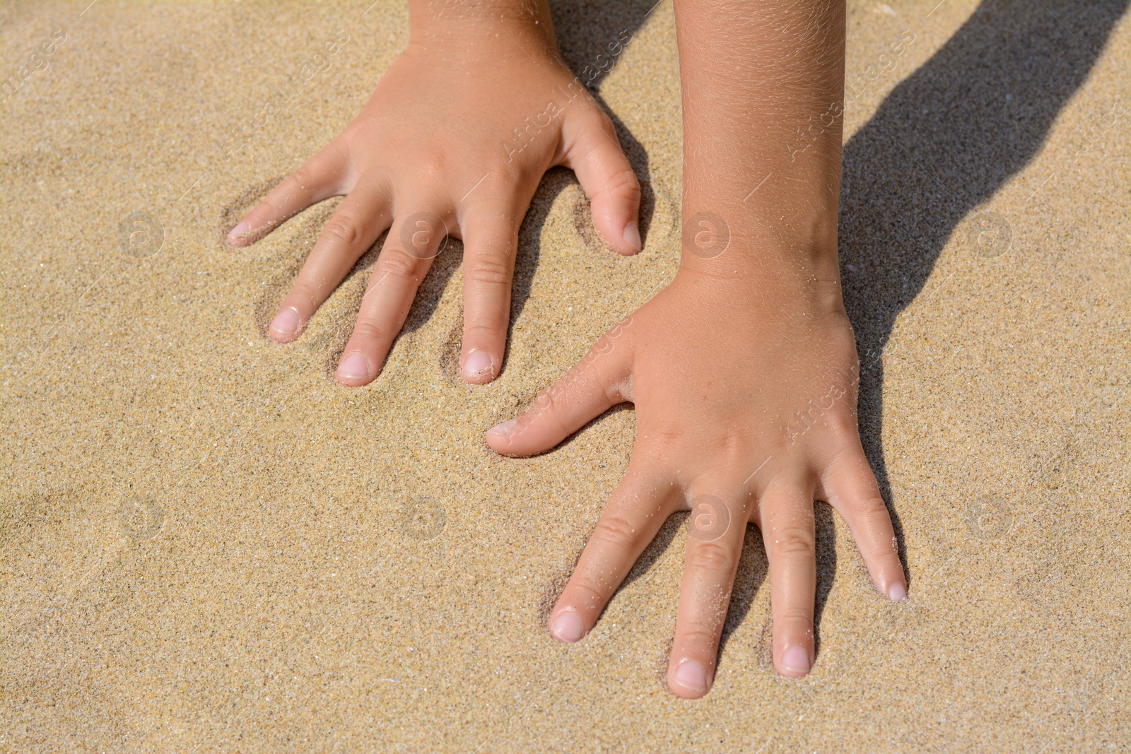 Photo of Child leaving handprints on sand outdoors, closeup. Fleeting time concept