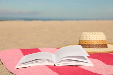Open book, hat and striped towel on sandy beach near sea. Space for text
