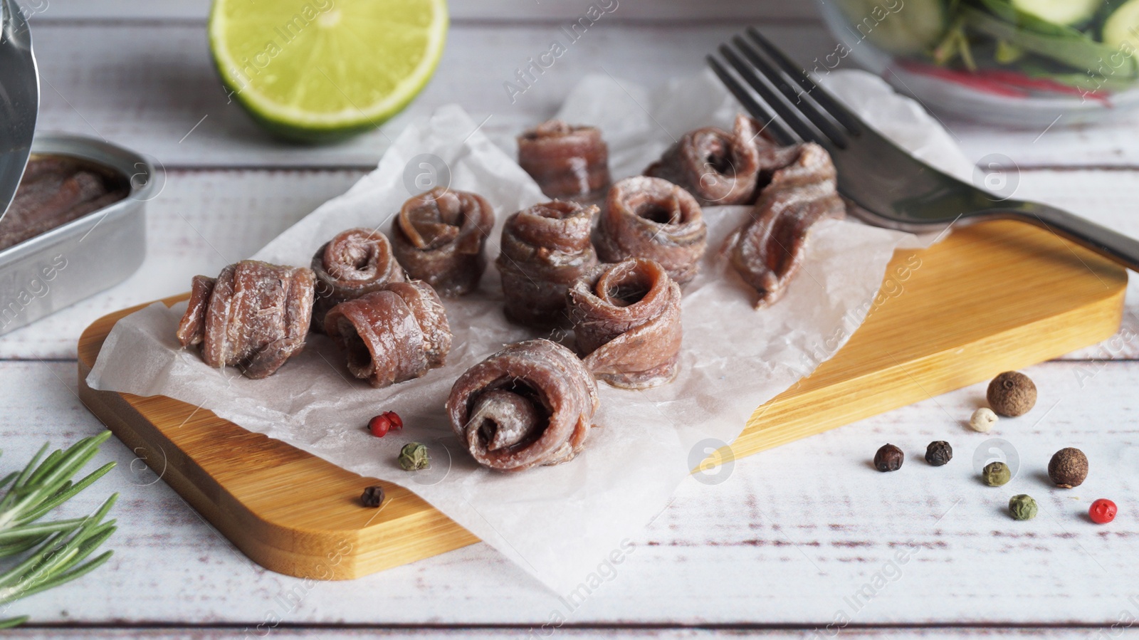 Photo of Canned anchovy fillets, rosemary and lime on white wooden table