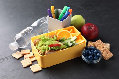 Lunch box with healthy food for schoolchild and markers on black textured table