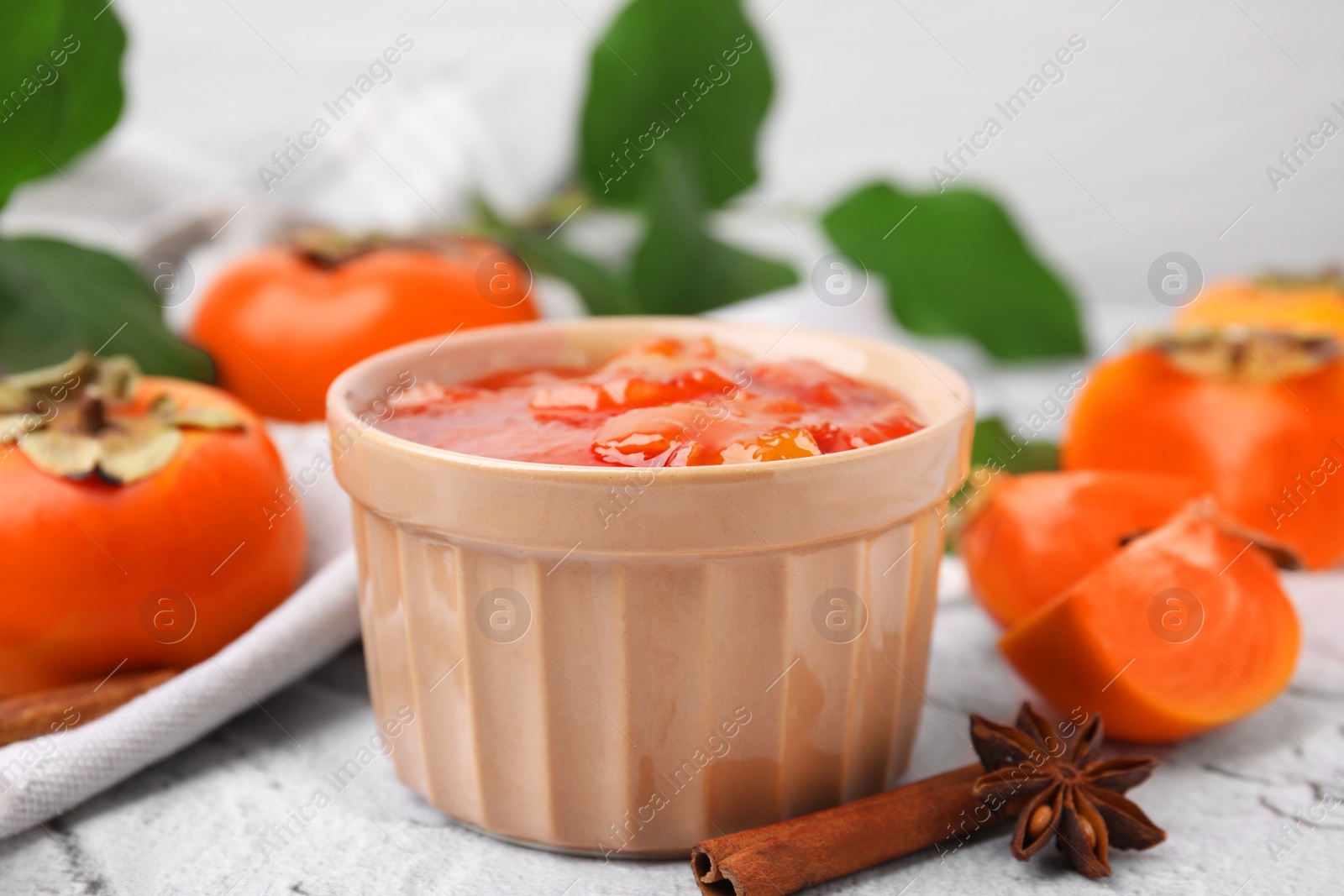 Photo of Bowl of tasty persimmon jam and ingredients on white textured table, closeup