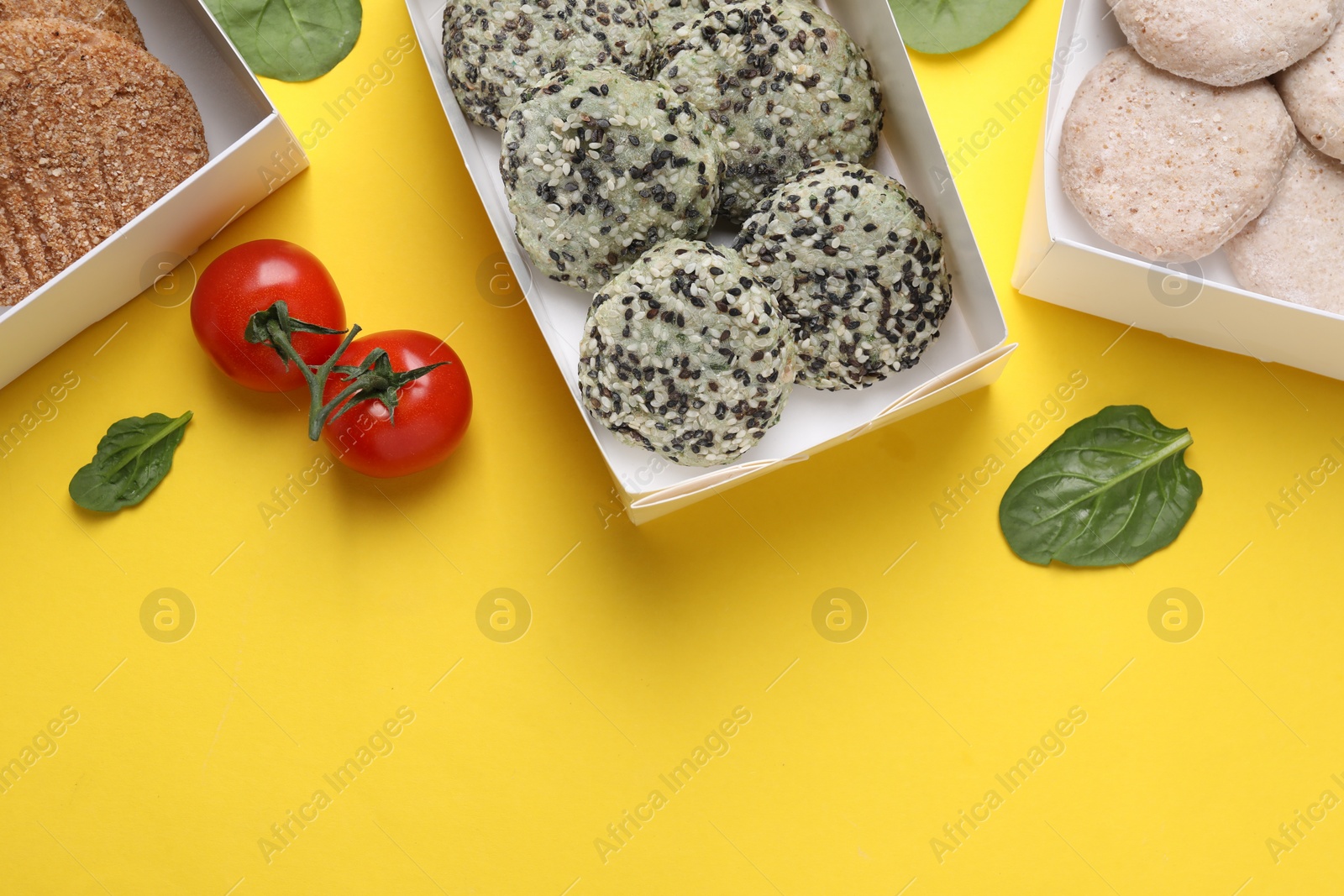 Photo of Many different raw vegan meat products, tomatoes and spinach on yellow background, flat lay. Space for text