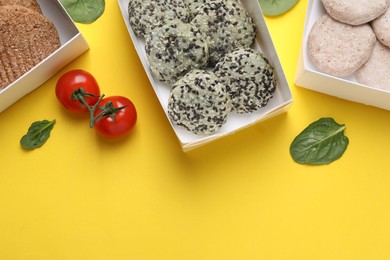 Many different raw vegan meat products, tomatoes and spinach on yellow background, flat lay. Space for text