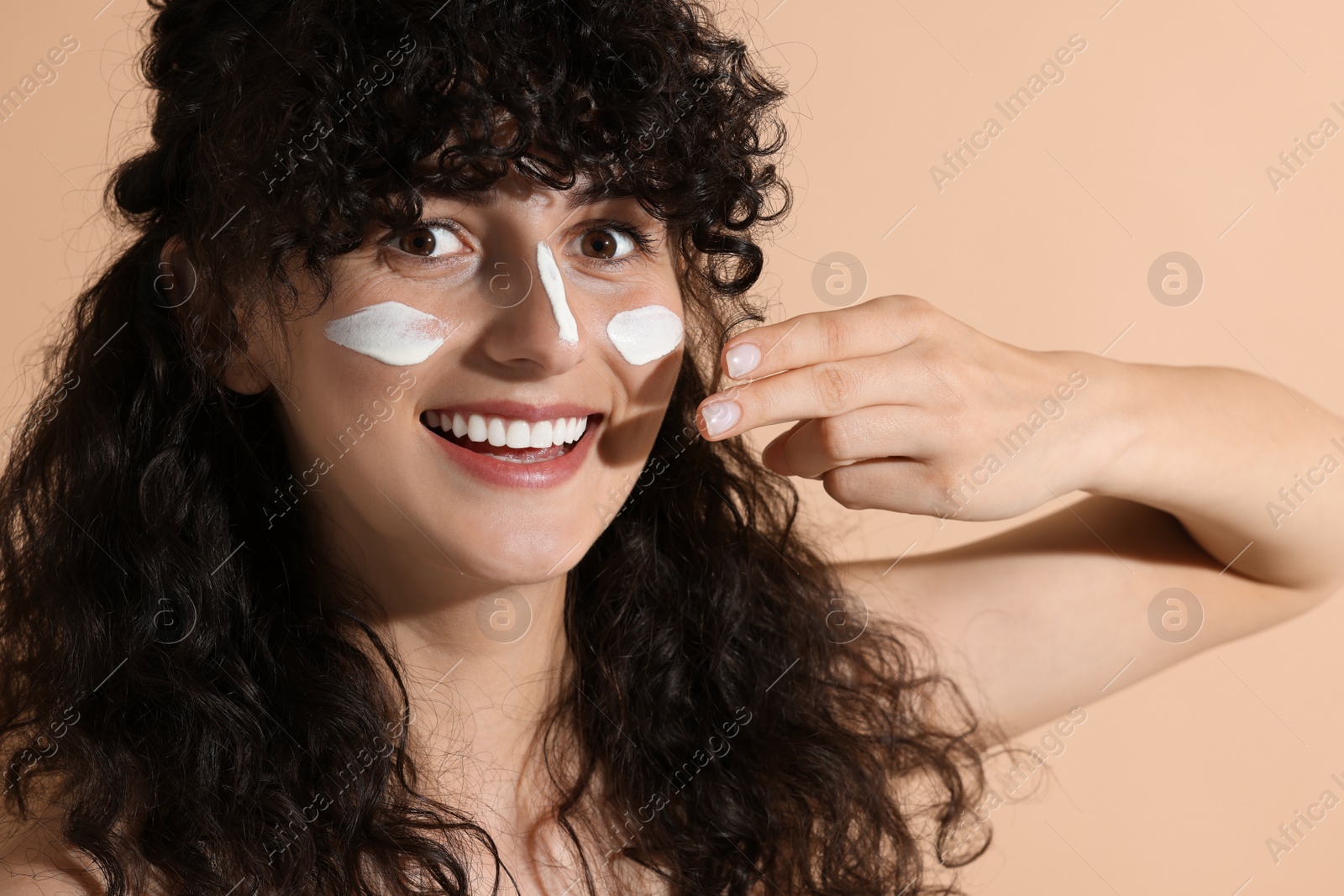 Photo of Beautiful young woman applying sun protection cream onto face on beige background