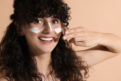 Beautiful young woman applying sun protection cream onto face on beige background