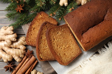 Photo of Delicious gingerbread cake, ingredients and fir branches on wooden table, flat lay