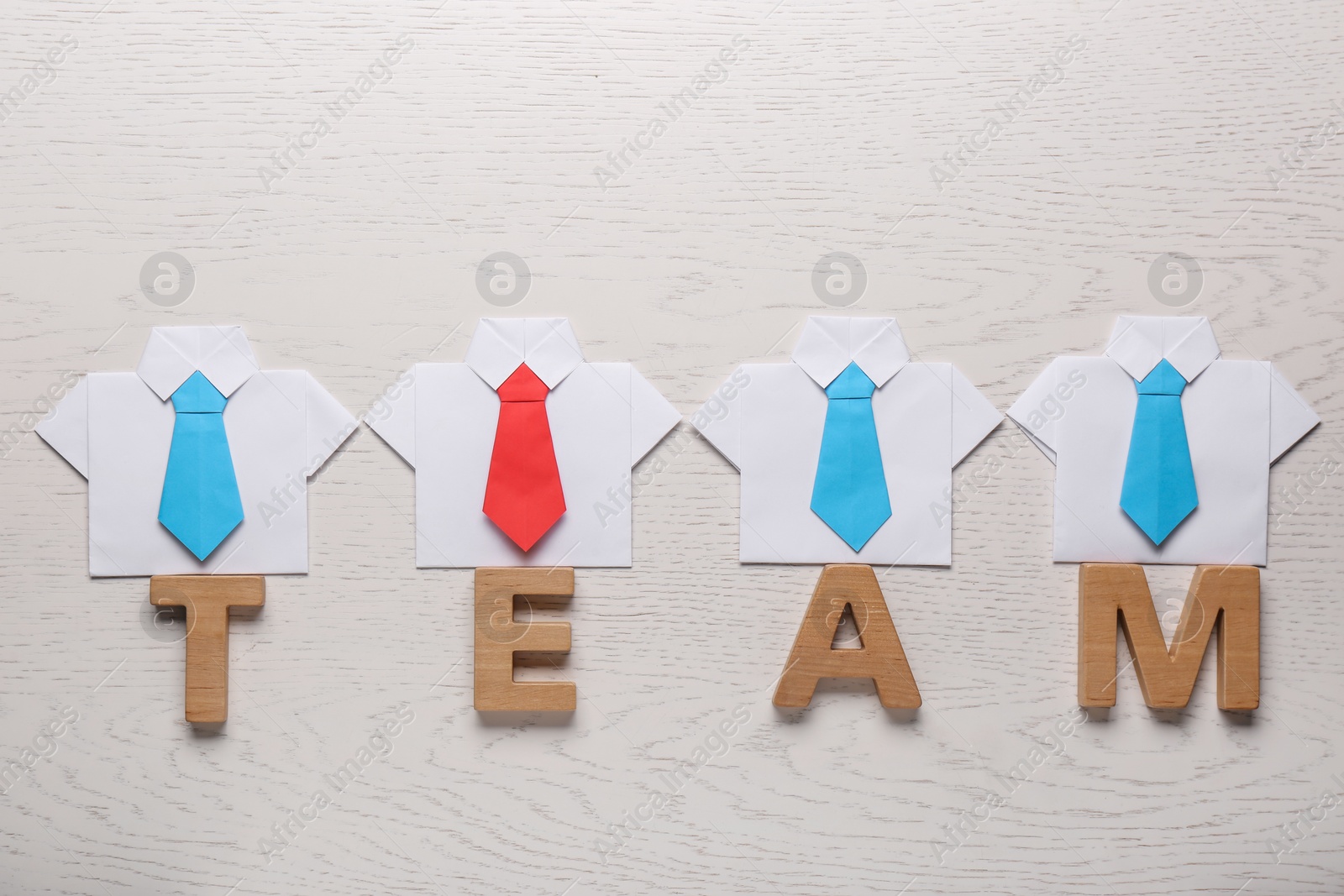 Photo of Many paper shirts and word Team on white wooden background, flat lay. Recruiter searching employee