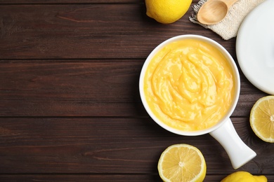 Delicious lemon curd in saucepan on dark wooden table, flat lay. Space for text