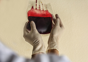 Woman holding blood for transfusion on beige background, closeup. Donation concept