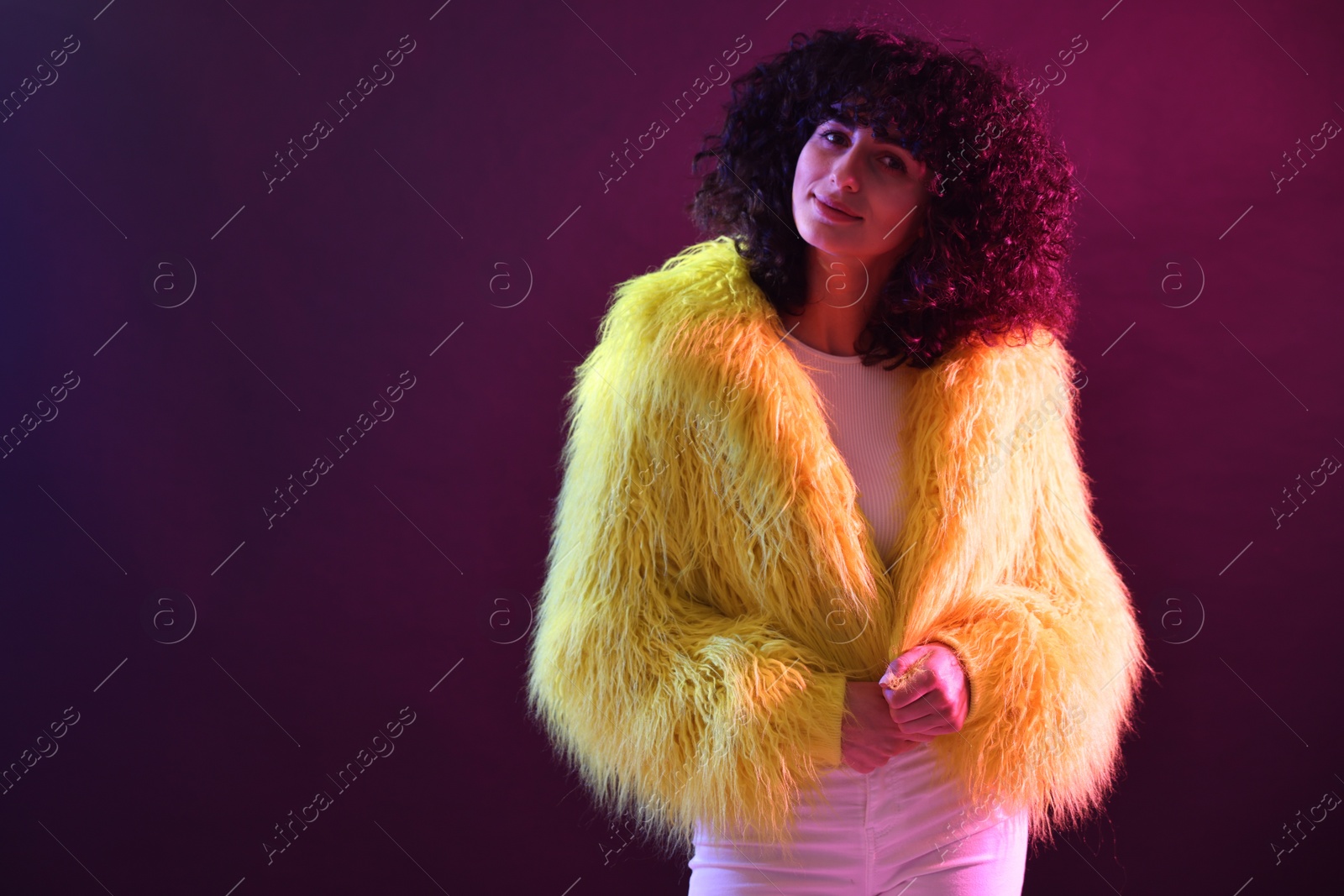 Photo of Beautiful young woman in yellow fur coat and sunglasses on color background in neon lights