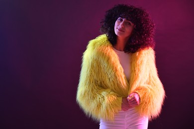 Photo of Beautiful young woman in yellow fur coat and sunglasses on color background in neon lights