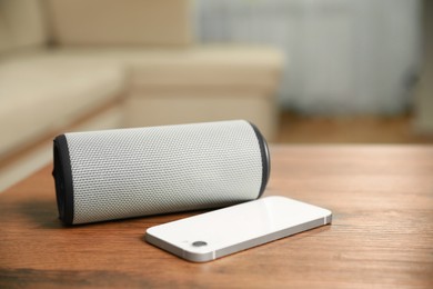 Photo of Portable bluetooth speaker and smartphone on wooden table indoors, space for text. Audio equipment