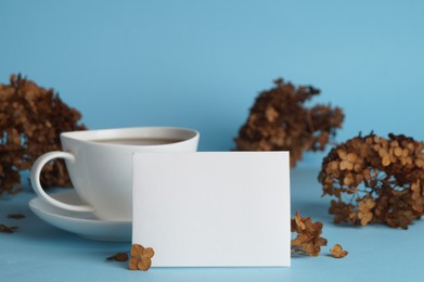 Photo of Dried hortensia flowers, sheet of paper and cup with coffee on light blue background. Space for text