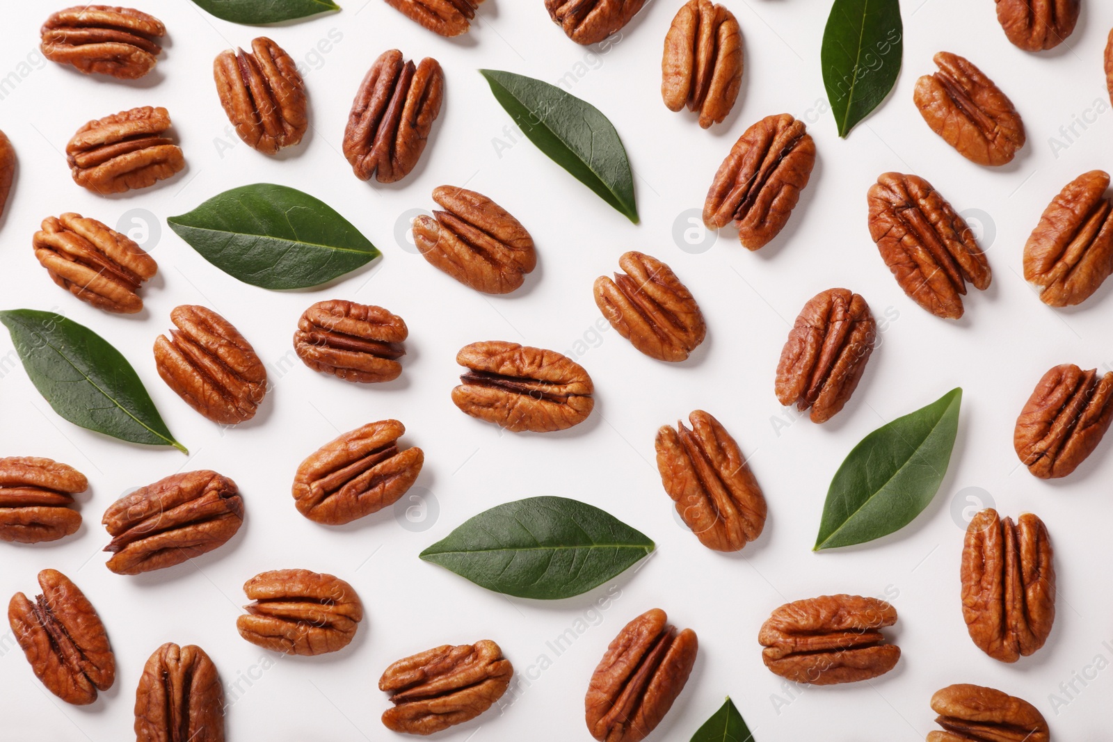 Photo of Delicious pecan nuts and green leaves on white background, flat lay