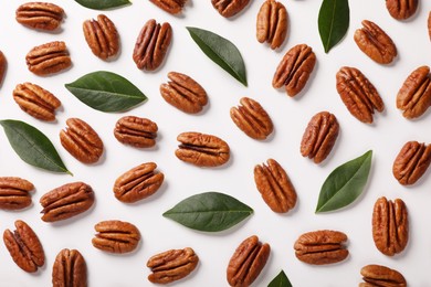 Delicious pecan nuts and green leaves on white background, flat lay
